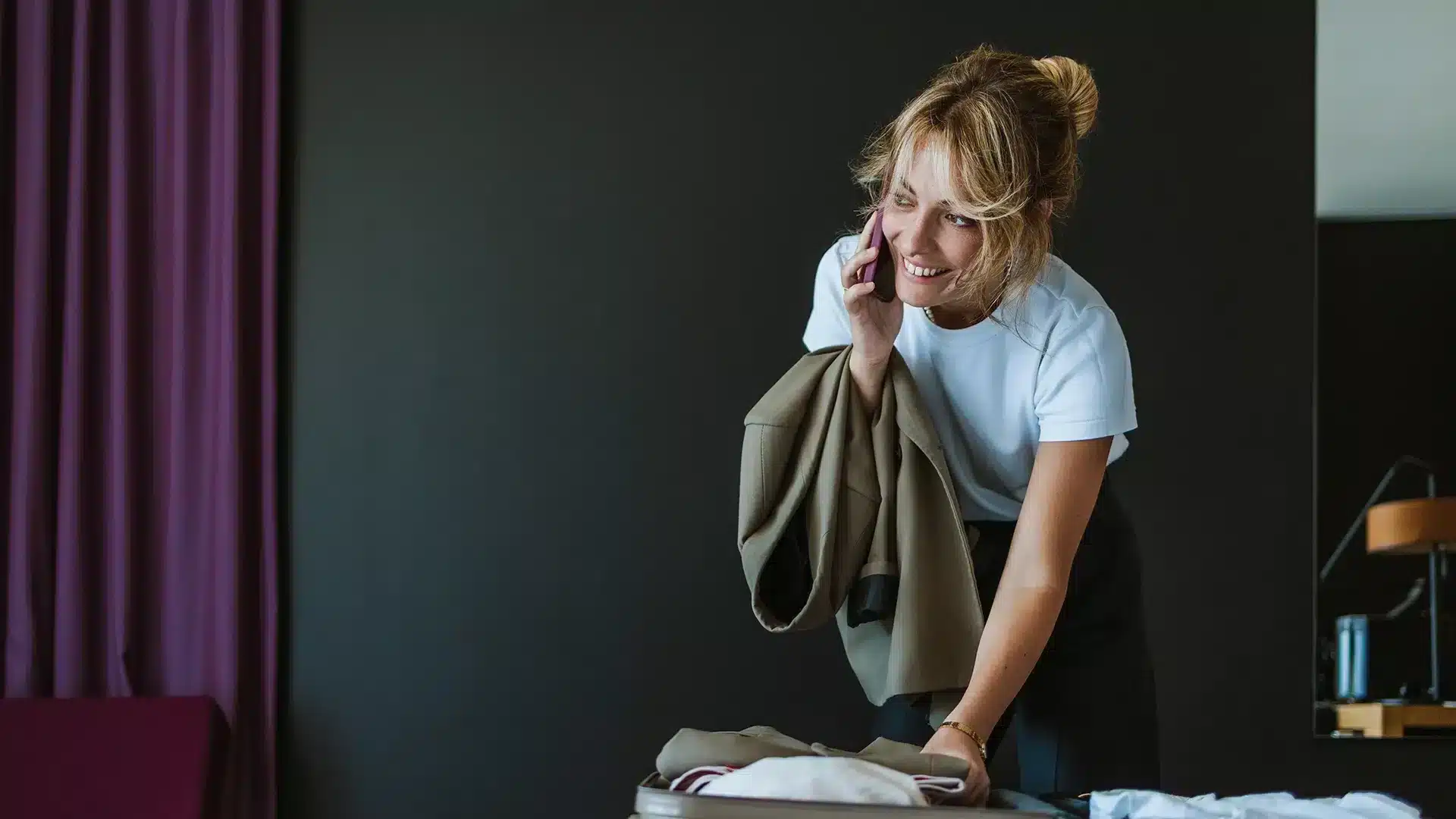 Frau telefoniert im Hotelzimmer und packt dabei ihre Koffer